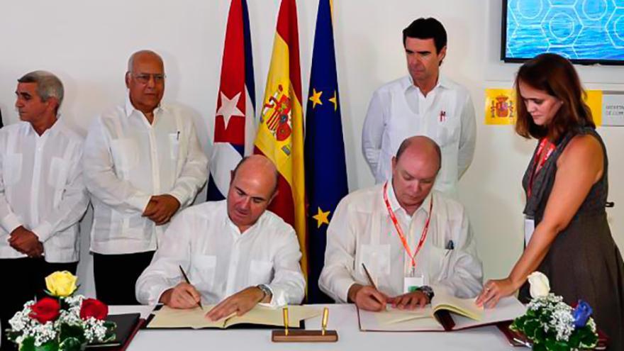 El ministro de Economía y Competitividad, Luis de Guindos (izq.), y el ministro cubano de Comercio Exterior e Inversión Extranjera, Rodrigo Malmierca (der), firman acuerdos de cooperación en La Habana en presencia del ex ministro de Energía y Turismo, José Manuel Soria (de pie). (EFE)