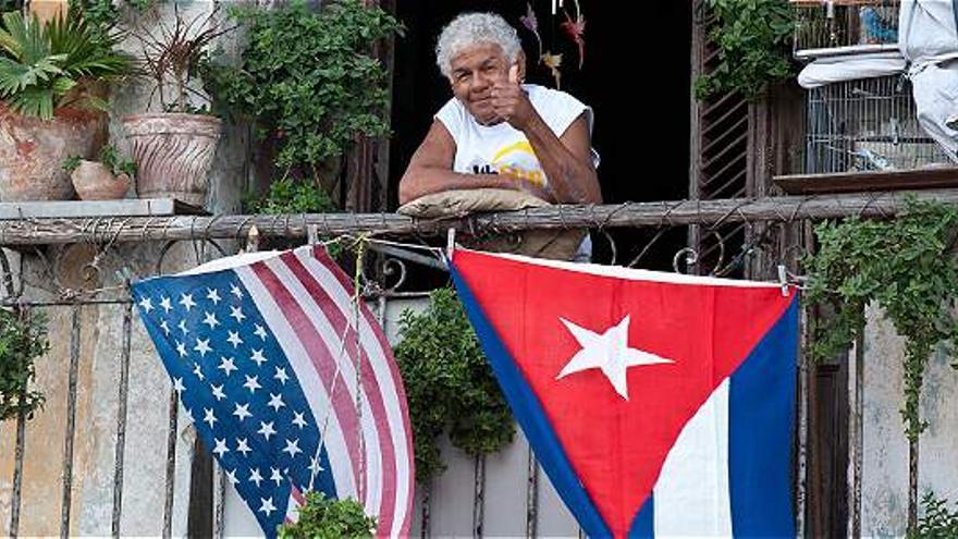 Una señora desde su balcón saluda con las banderas de Cuba y Estados Unidos ondeando hacia afuera. (EFE)