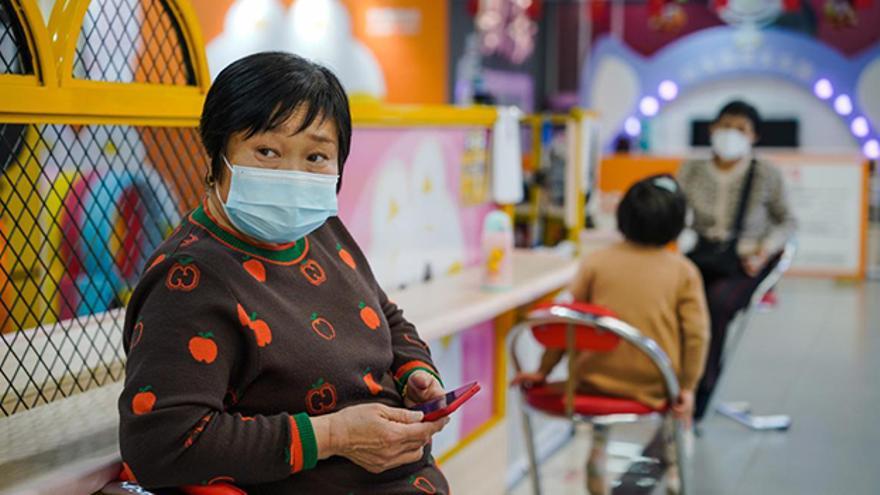 Una mujer protegida con una mascarilla utiliza su móvil en un centro comercial de Pekín. (EFE)