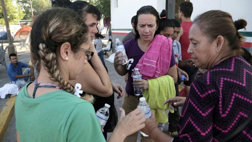 Una voluntaria mexicana, a la derecha, da agua a mujeres migrantes cubanas que viven en un campamento improvisado junto al Puente Internacional en Matamoros, México. (el Nuevo Herald)